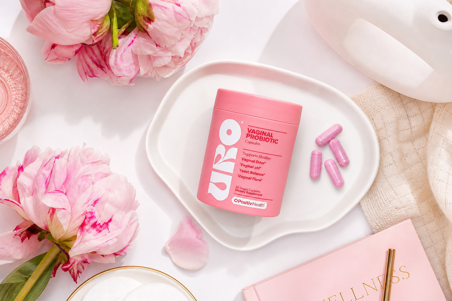 Flatlay editorial con MYUROCARE.COM, flores y cápsulas rosadas